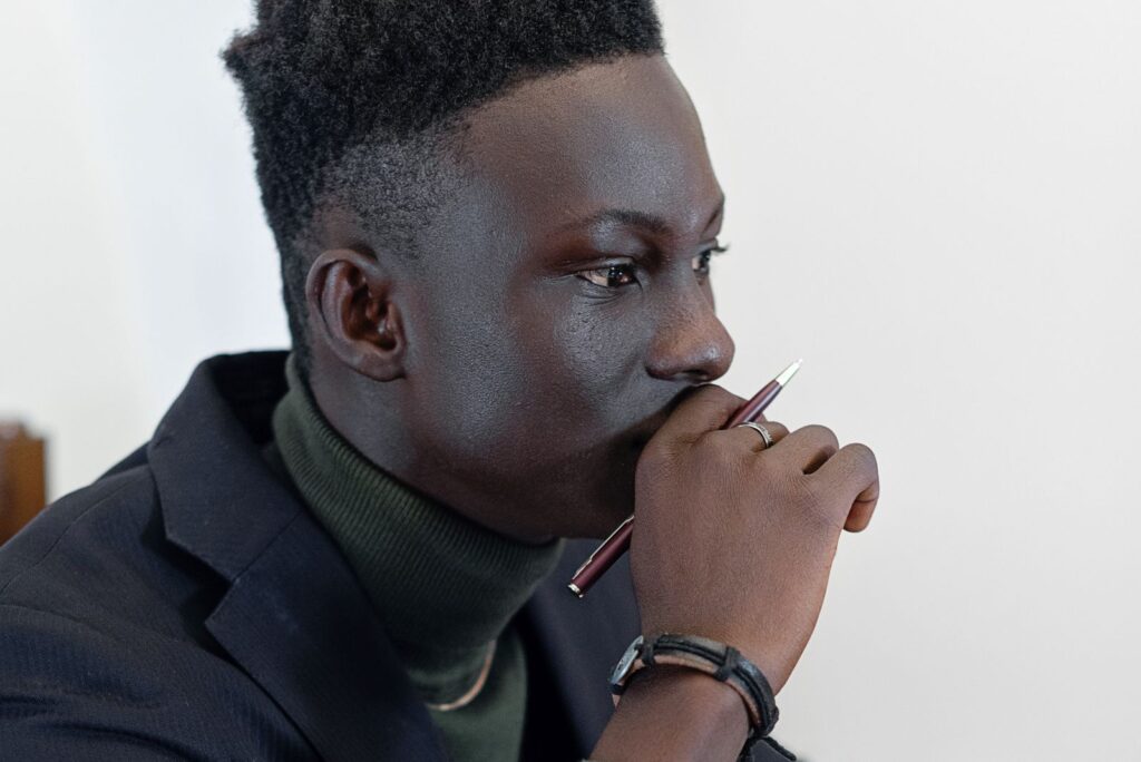 Thoughtful African man holding a pen, deep in thought in an office