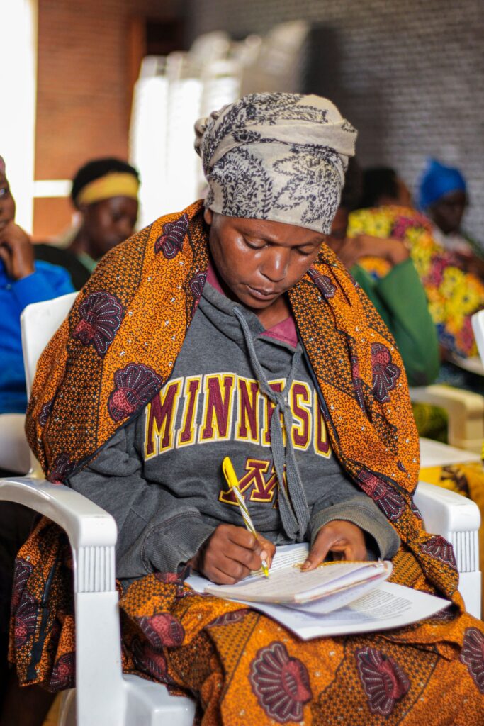 African woman in colourful attire taking notes during a community session